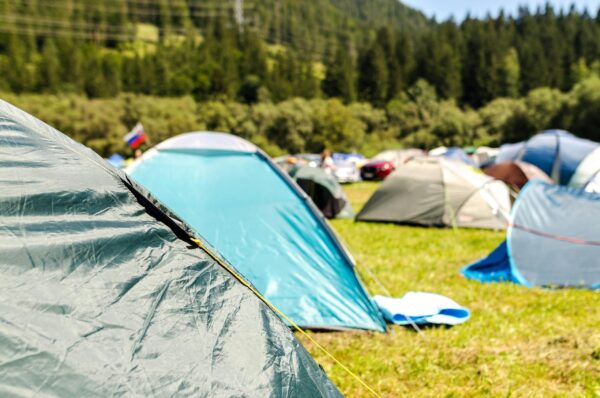 Vibrant camping tents set up in a lush forest landscape under a sunny sky.